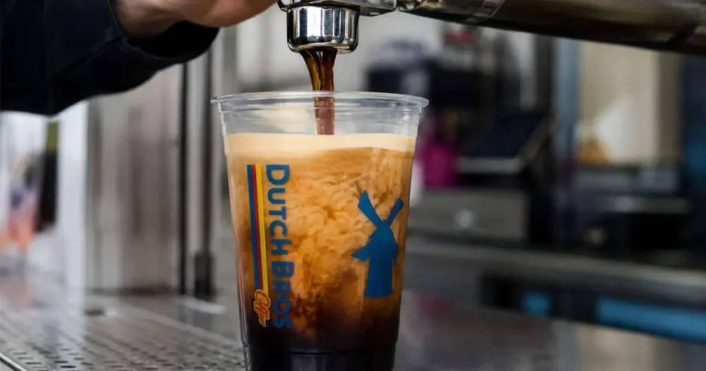Dutch Bros Nitro Cold Brew cascading into a clear cup showing frothy crema-like head and dark coffee body.